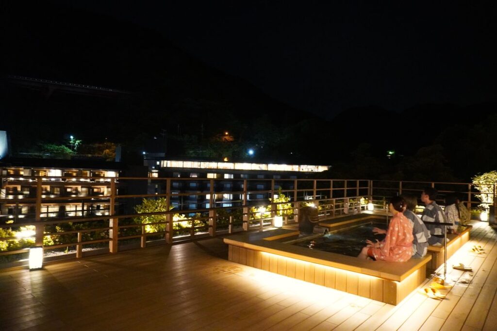 Guests relaxing in a rooftop foot bath at a ryokan in Hakone-Yumoto at night