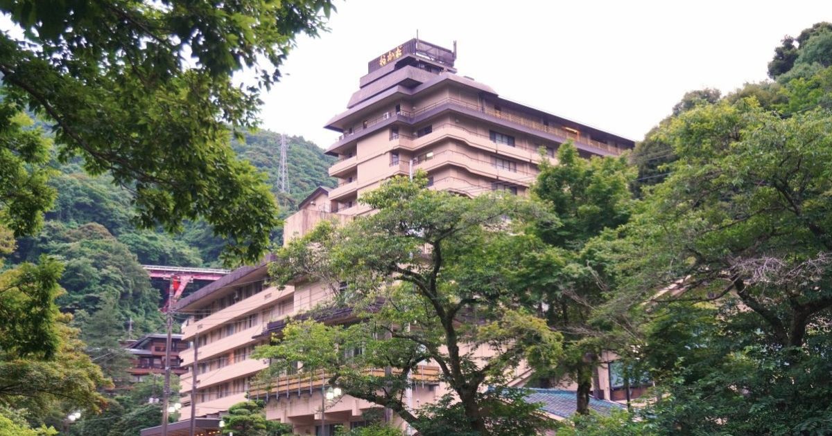 Exterior view of Hotel Okada, a large hot spring ryokan surrounded by the lush green mountains of Hakone.